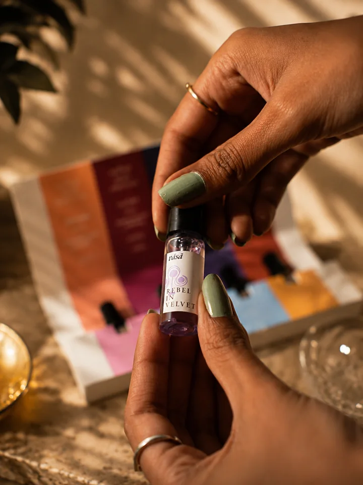 Hands holding the Rebel in Velvet vial, its juice pale lilac, its label marked with a lilac swirl, before the open kit