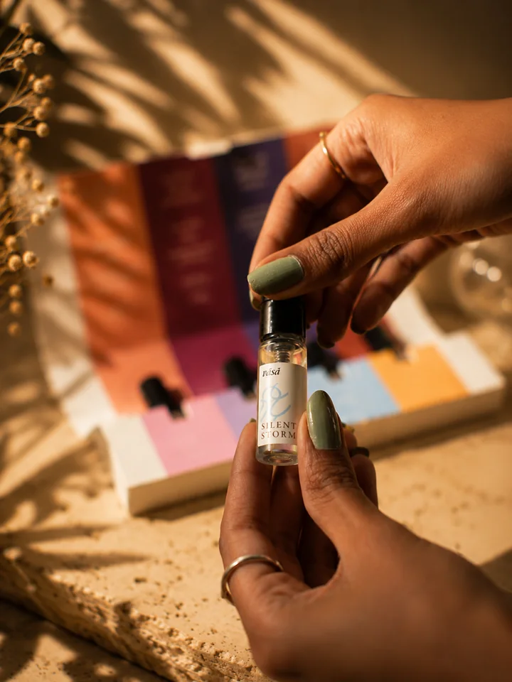 Hands holding the clear Silent Storm vial over the open kit, with dried baby's breath and sunlit stone