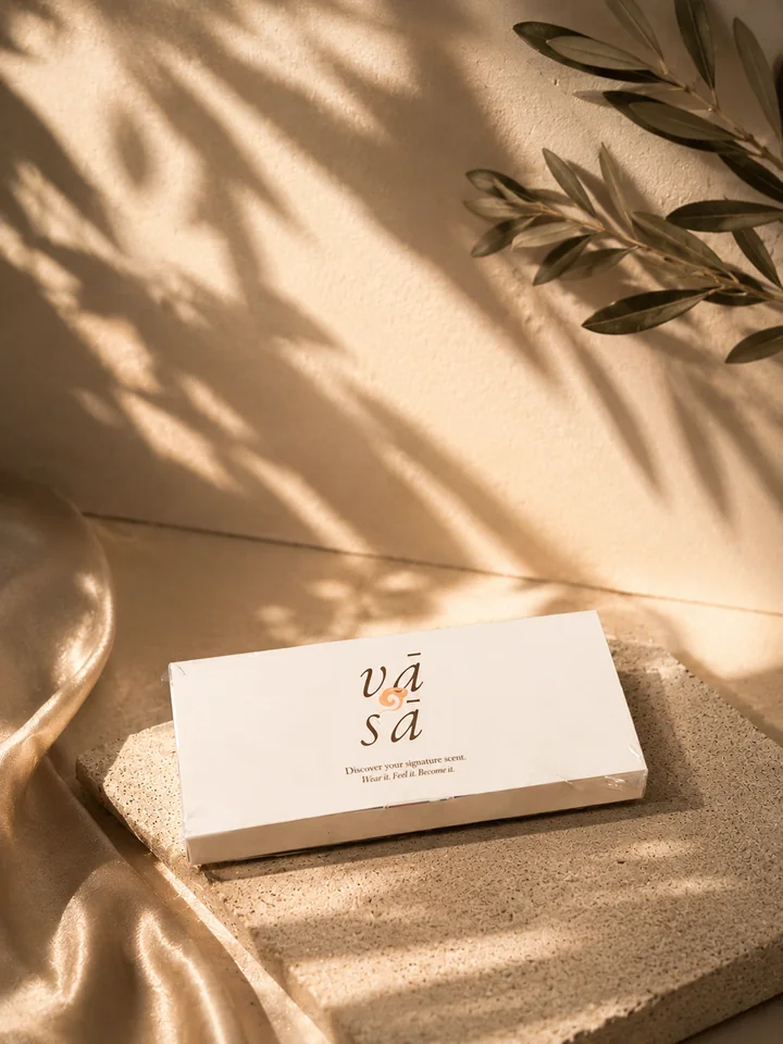 The Discovery Kit closed in its ivory sleeve with the vā sā mark, on a stone slab beside pale satin, olive leaves and their shadows on a cream wall
