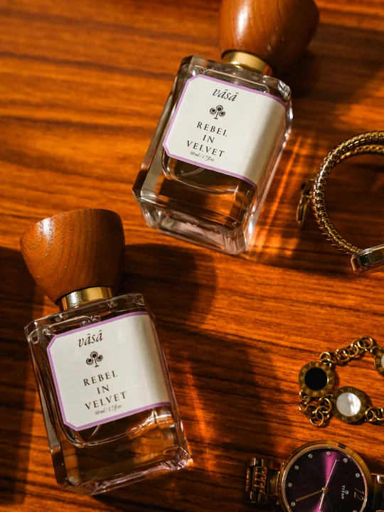 Two bottles of Rebel in Velvet on a warm wooden table among gold bracelets and a watch