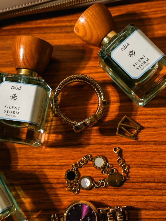 Two bottles of Silent Storm on a warm wooden table among gold bracelets and a watch